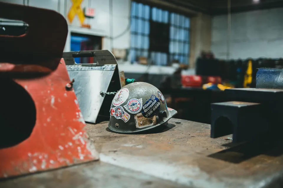 A safety helmet with stickers on a bench inside an industrial workshop.