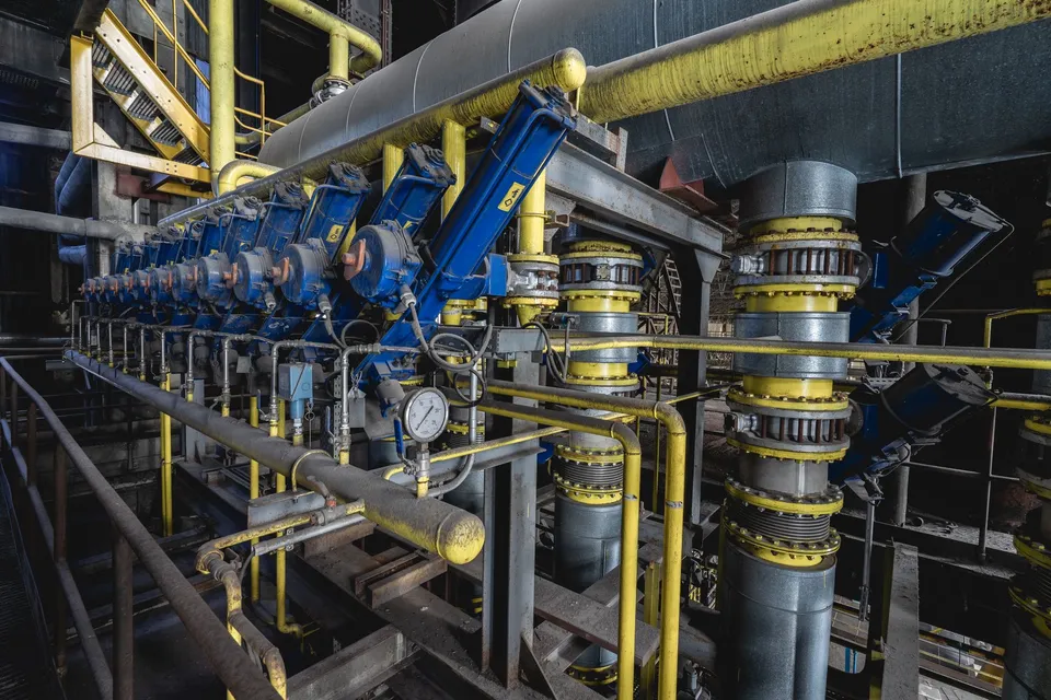 A detailed view of an industrial machine room featuring complex blue and yellow equipment and piping.