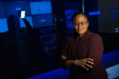 Professional woman standing confidently in a data center, surrounded by glowing servers.