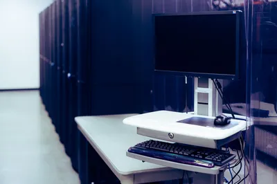 Contemporary computer with black screen placed on stand near row of server steel racks in data center