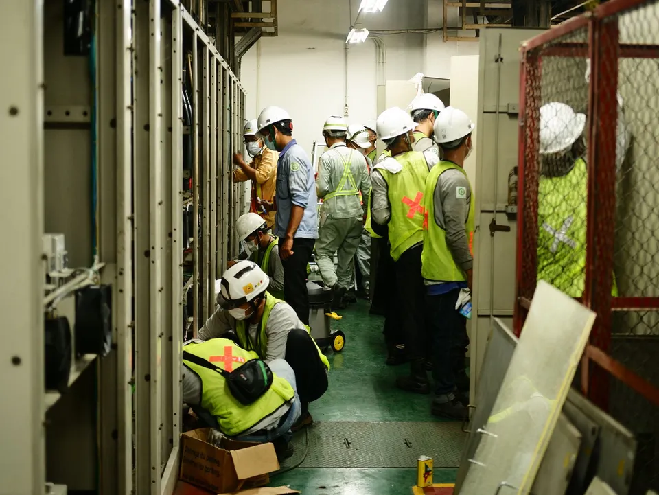 Group of construction workers in an industrial room, wearing helmets and safety vests, working together.