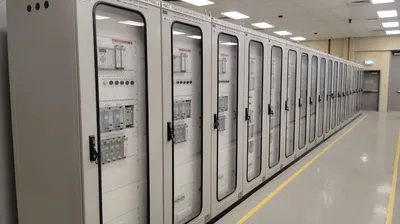 View of an industrial control room featuring rows of electrical panels in a well-lit environment.